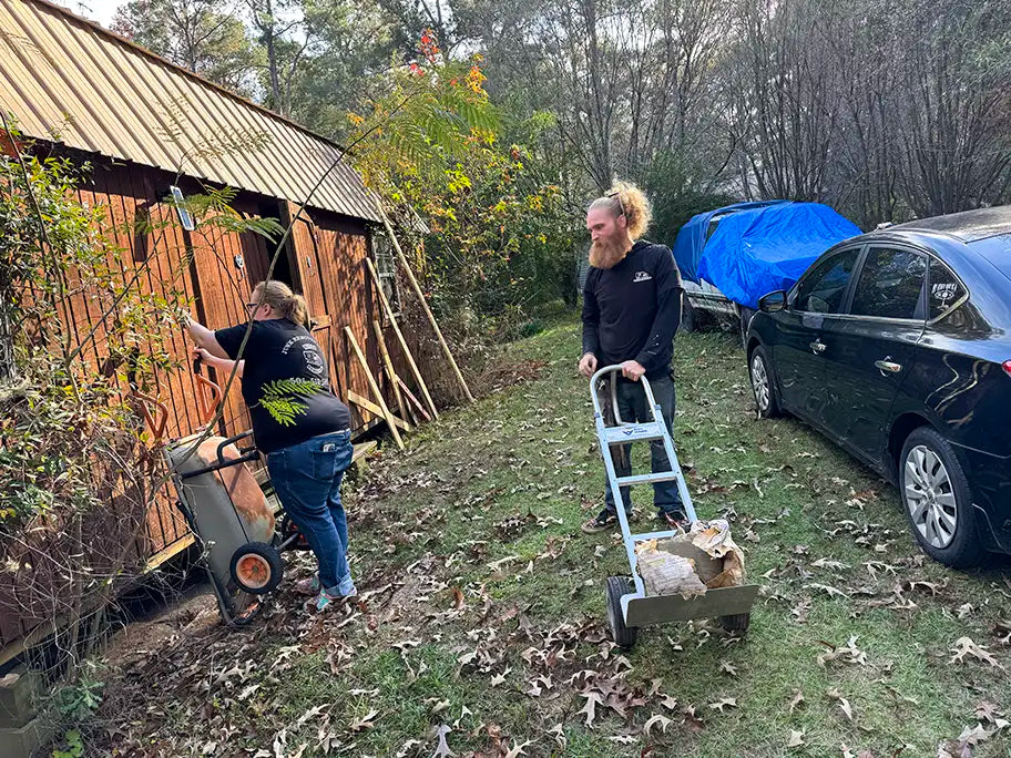 Two people, one using a wheelbarrow and other using a moving dolly to move items 