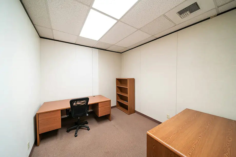 Empty office room with wooden desk, chair, and bookshelf.